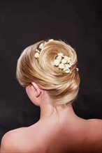 View from behind of a stylish woman with an elegant blonde hairstyle with her hair coiffed in a neat knot with a floral hair accessory and bare shoulders