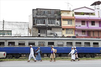 Muslim men walk in front of a train at the railway station in Trang Town
