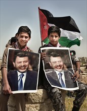 Two boys in scout uniform with portraits of Jordans King Abdullah II bin al-Hussein in front of the Jordanian flag. Amman