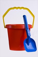 A bright red plastic childs bucket with a yellow handle and a blue spade