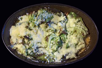 Kale gratinated with cheese and minced meat in an earthenware casserole on a black background