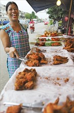 Laughing Thai woman with grilled chicken on a spit