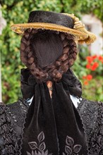Beautiful hairstyle of a German woman in a traditional shawl with her neatly braided and tied brunette hair and hat with a black bow