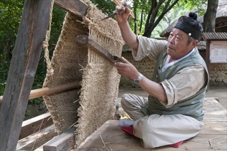 Man weaving a straw floor mat with a traditional loom