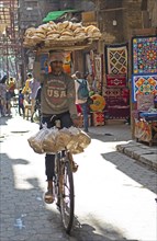 Egyptian man with pita bread on his head riding bicycle in bazaar