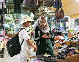 Shopping in the market: two young woman in hats and headscarves looking at a mobile phone. Aqaba