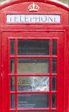 Smashed vandalised glass panel of old red telephone box