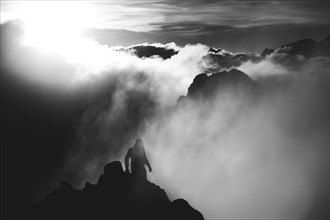 A climber walking along a ridge during a sunrise in the clouds