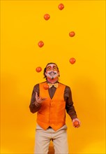 Portrait of a juggler in a vest with a painted face juggling balls on a yellow background