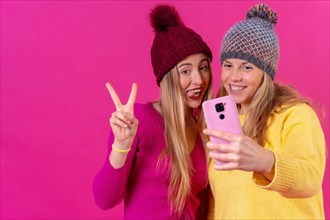 Two young blonde caucasian women with a phone isolated on a pink background