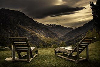 Deck chairs on a mountain meadow with autumnal mountain forest and threatening cloudy sky