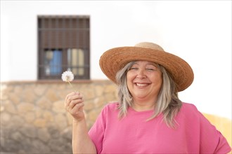 Woman with hat and white hair smiling with a dandelion in her hand