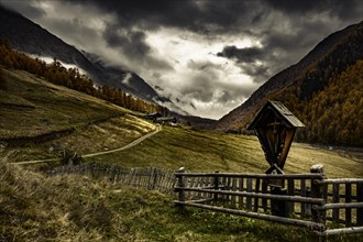 Way cross with alpine hut in autumnal mountain landscape with threatening cloudy sky