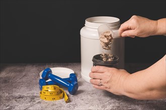 Woman pouring a scoop of protein powder in an insulated shaker on a black background