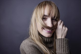 Young woman with long blond hair makes a moustache out of a strand of hair and smiles at camera