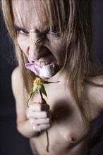 Young naked woman eating the petals of a rose and looking aggressively into the camera