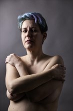 Nude woman with dyed hair crosses her arms in front of her chest