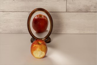 Bitten red apple reflected in a mirror isolated on a white table with copy space