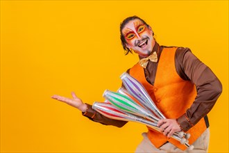 Happy juggler man in makeup vest juggling maces on a yellow background