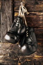 Old leather boxing gloves hanging in front of rustic wooden wall