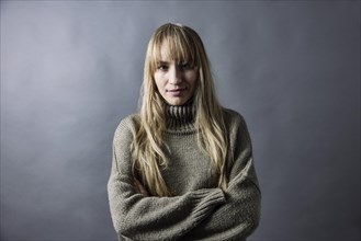 Woman with long blond hair and warm woollen jumper crosses her arms