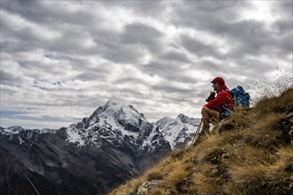 Mountaineer on autumnal mountain meadow with cloudy sky in front of Ortler summit massif