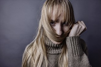 Young woman with long blond hair coquettishly holding a strand of hair in front of her mouth