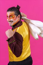 Juggler in a vest and with painted face juggling with maces on a pink background