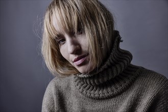 Young woman hides her long blond hair in a turtleneck jumper and looks seductively into camera