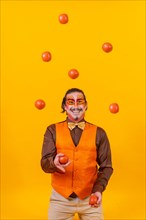 Juggler in a vest and with a painted face juggling balls on a yellow background