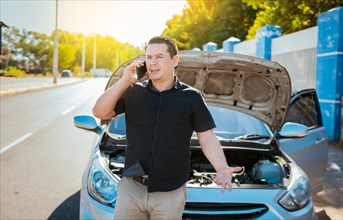 Young man with damaged car calling the mechanic. Driver with the damaged car calling the mechanic. Frustrated man with damaged car calling technician on the road