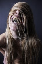 Young naked woman laughing covering her face with her wild long blond hair