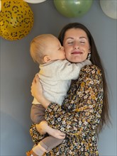 Young pretty mother is kissed on the cheek by her one year old son on his first birthday