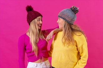 Two blonde caucasian women in wool hats on a pink background