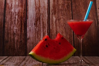 Cocktail glass with watermelon juice and slices of fresh watermelon on a wooden table