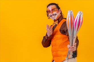 Portrait of a juggler in a vest with a painted face juggling with maces on a yellow background