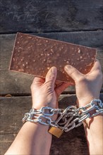 Woman holding a chocolate bar with her hands chained together as a dietary slave concept