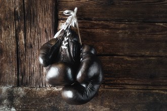 Old leather boxing gloves hanging in front of rustic wooden wall