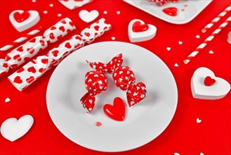 Red Valentines Day candy on plate surrounded by seasonal decoration