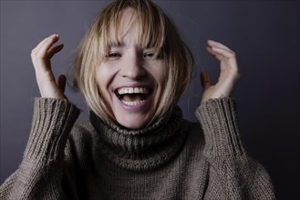 Young woman hides her long blond hair in a turtleneck jumper and laughs into camera
