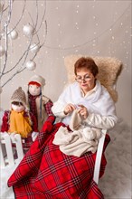 A nice elderly woman sews to knit her granddaughters in a Christmas arrangement. In studio