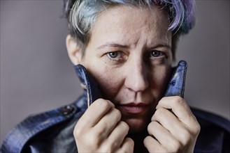 Androgynous woman with dyed hair pulls up the collar of her denim jacket