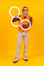 Happy juggler man in makeup vest juggling hoops on a yellow background