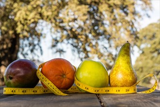 Group of healthy fruit with tape measure on a wooden table illuminated by the sun