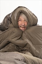 Elderly gentleman freezing and shivering in sleeping bag