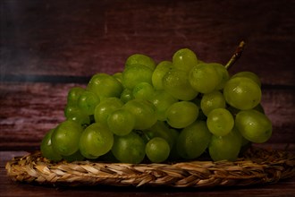 Close-up of a bunch of green grapes on an esparto grass tray with a dark wood background