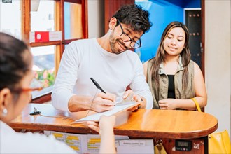 Couple signing in at a hotel reception. Young couple signing documents in a hotel reception. Latin couple signing reservation at hotel reception. Hotel reservation concept