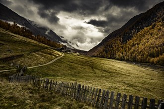 Wooden fence with alpine hut in autumnal mountain landscape with threatening cloudy sky