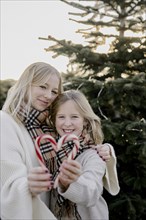 Two girls with candy cane hearts in front of a Christmas tree