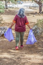 Woman seen from the back carrying bags of garbage collected in the field
